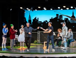 An image of the full cast of Peter & the Wolf gathered onstage for a curtain call, with Isaac Mizrahi and John Heginbotham acknowledging the audience in front of the city skyline backdrop.