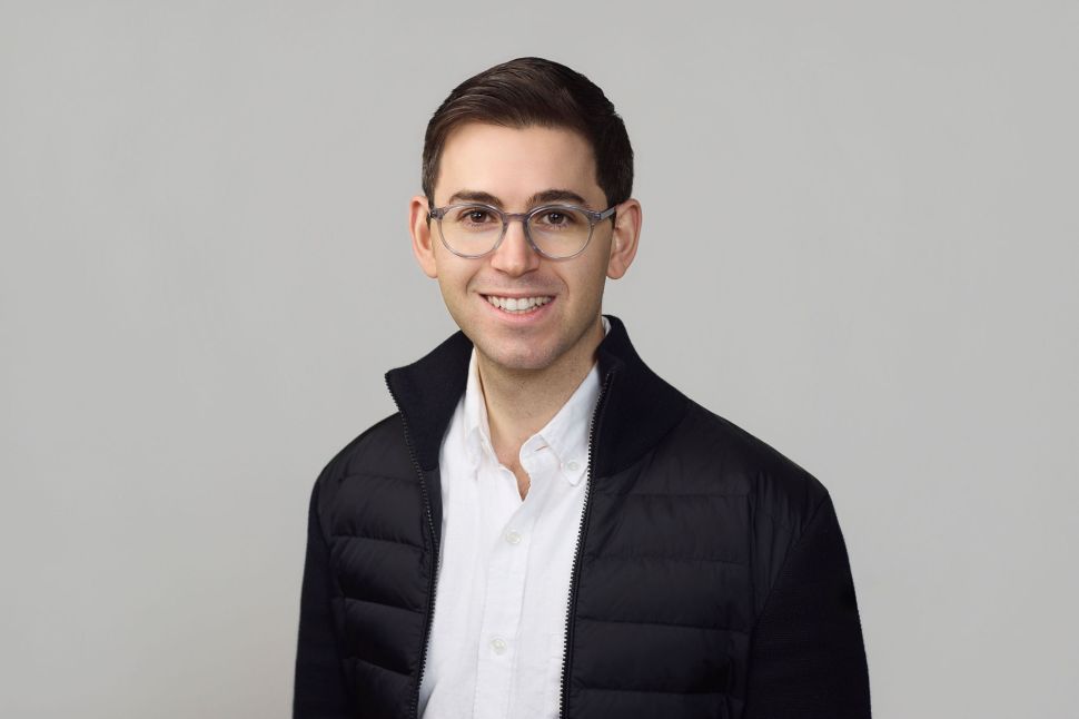 Headshot of man in black jacket and white shirt, wearing glasses