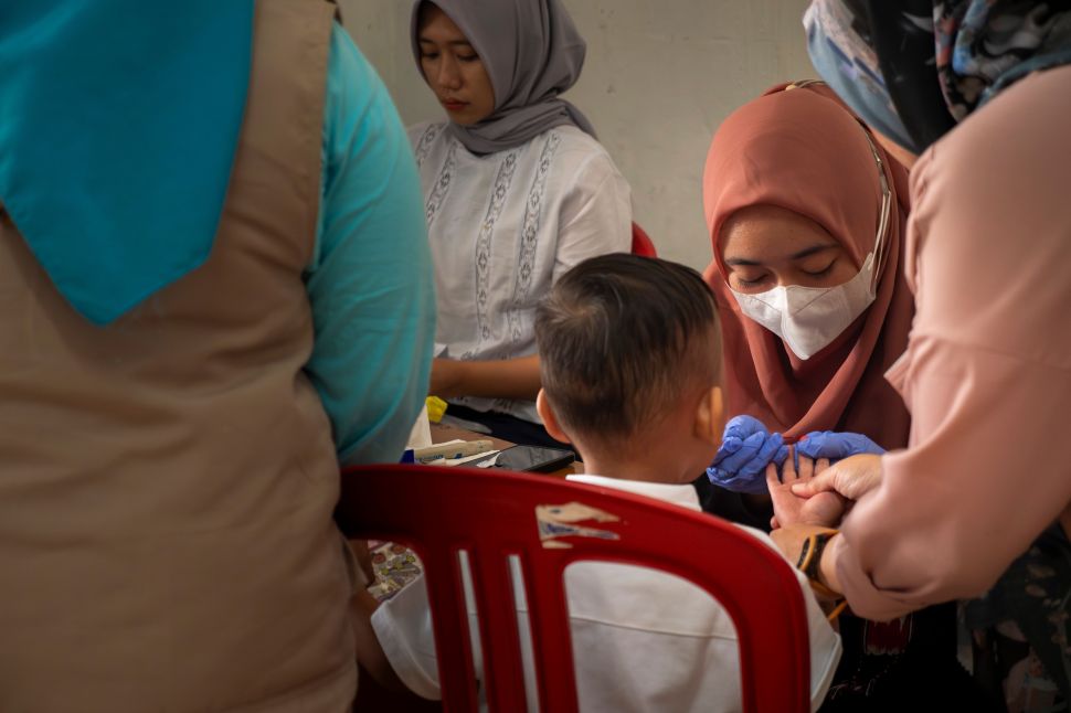 A woman in a mask administers a blood lead level test to a child