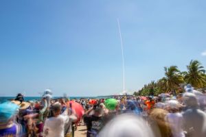 Spectators watch a rocket launch on a beach.