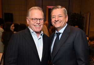 Two men wearing suits pose in room