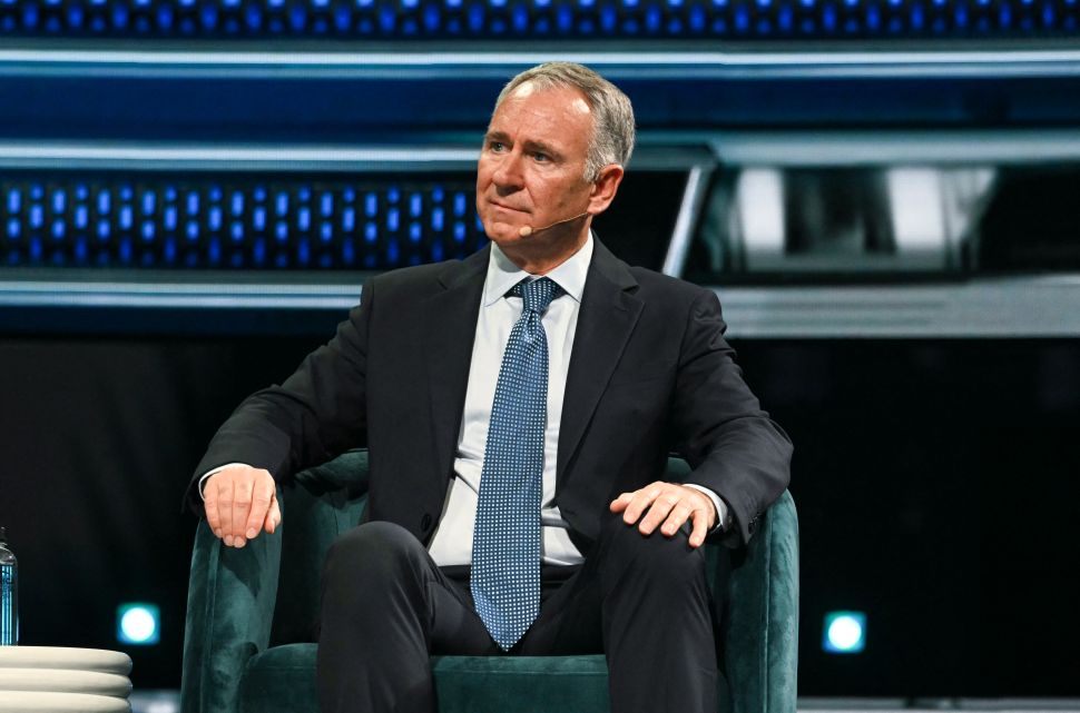 Man in suit and tie sits in chair onstage