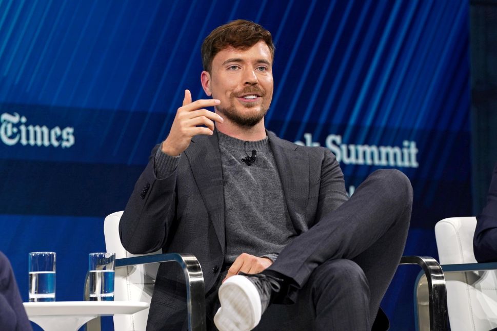 Man in grey blazer sits onstage in chair