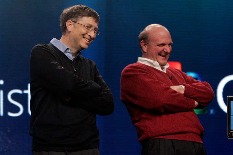 Two men, one in black sweater and one in red, stand onstage