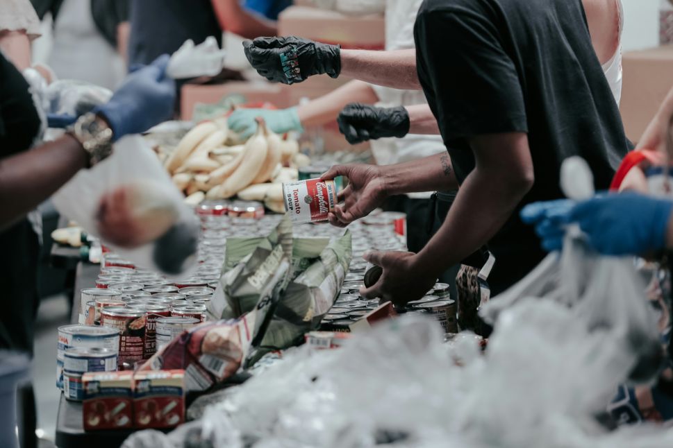 A man in a black t-shirt hands over a can of Campbell's soup at a food bank